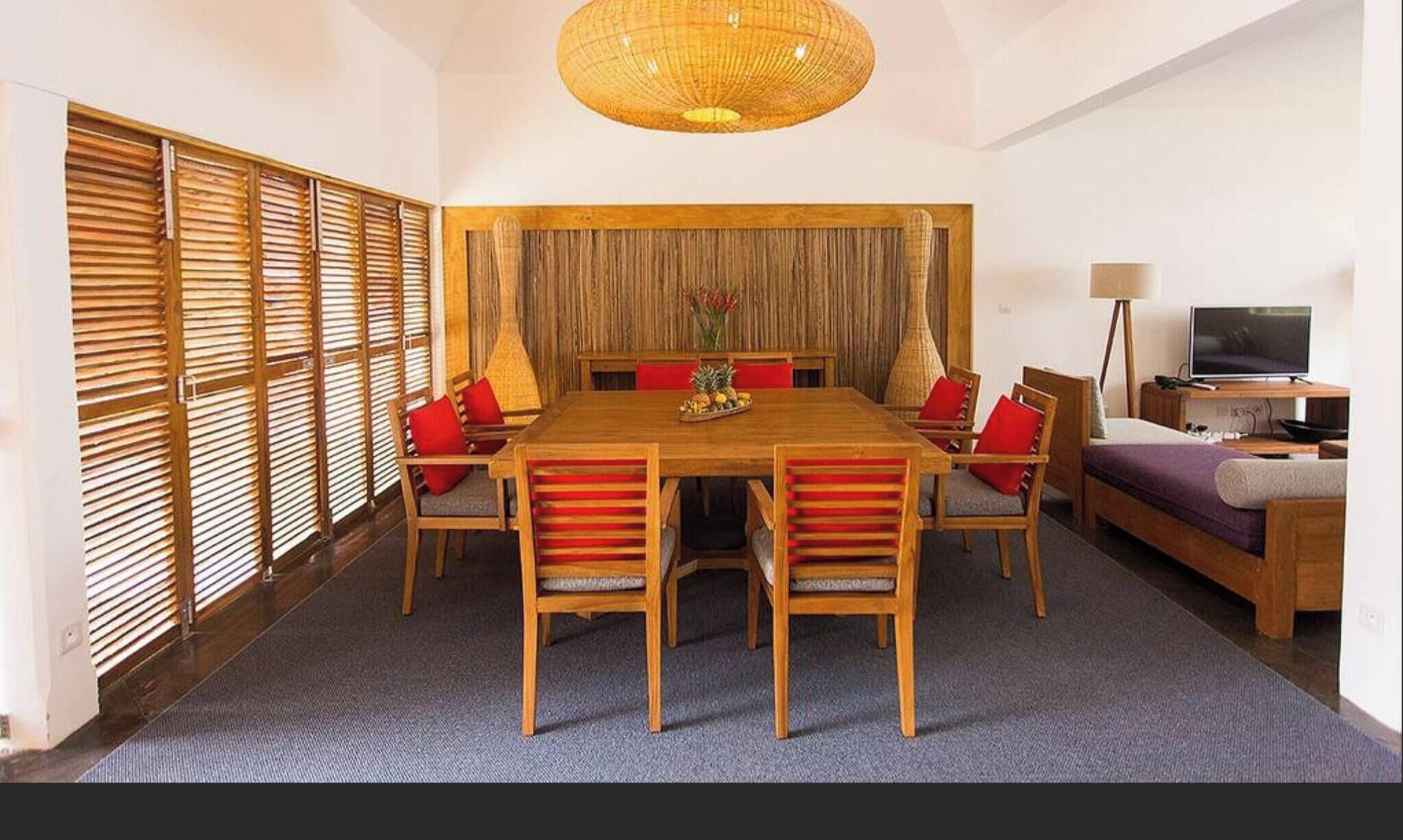 A room with a wooden dining table, chairs, a sofa, a television, and a lamp.