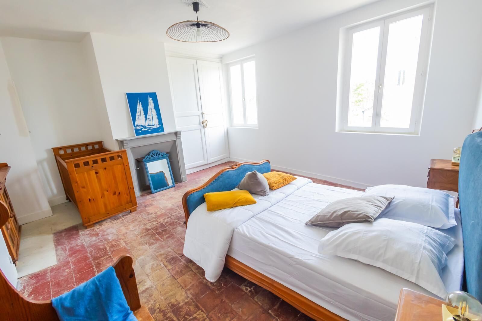 Un dormitorio con una cama, un cofre de madera, un espejo, una chimenea y una ventana.