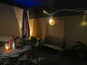 An outdoor patio with a table, chairs, a bench, and string lights. - La Parenthèse d’Honfleur Cosy | 2 Bedrooms & Private Courtyard (La Rivière-Saint-Sauveur)