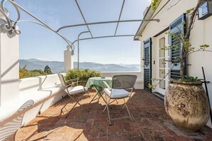 Eine Terrasse mit Tisch und Stühlen, einem Blumentopf und Blick auf Berge.