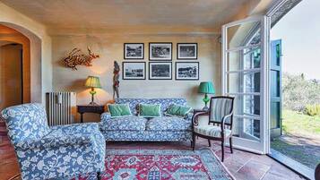 Een woonkamer met een gestreept bankstel, fauteuils, een rood tapijt met dessin en een wand met ingelijste foto's.