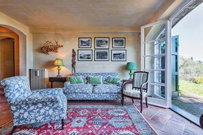 Un salon avec un canapé à motifs, des fauteuils, un tapis rouge à motifs et un mur orné de tableaux encadrés.