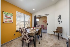 A dining area with a wooden table and chairs, a window with blinds, and a wall with a sign advertising Mexican cuisine. - The Chile Pad is a charming remodeled 3 bedroom, 2 bathroom townhouse. (Las Cruces)