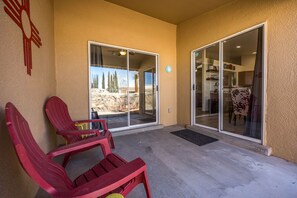 A covered outdoor area with two sliding glass doors leading to a patio, a concrete floor, and red plastic chairs. - The Chile Pad is a charming remodeled 3 bedroom, 2 bathroom townhouse. (Las Cruces)