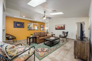 A living room with a brown sofa, a coffee table, a patterned rug, and a ceiling fan. - The Chile Pad is a charming remodeled 3 bedroom, 2 bathroom townhouse. (Las Cruces)