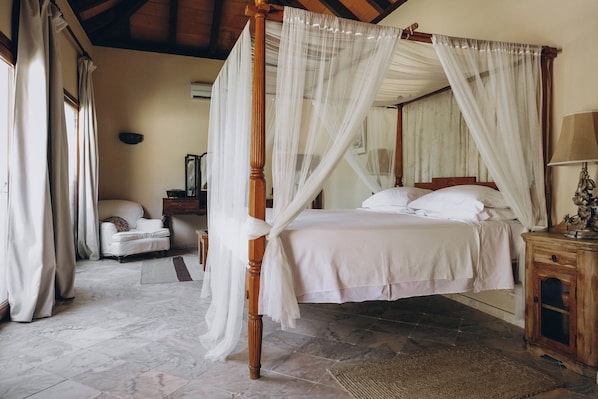 Una cama con dosel y cuatro postes, con ropa de cama blanca, una mesita de noche de madera y una silla.
