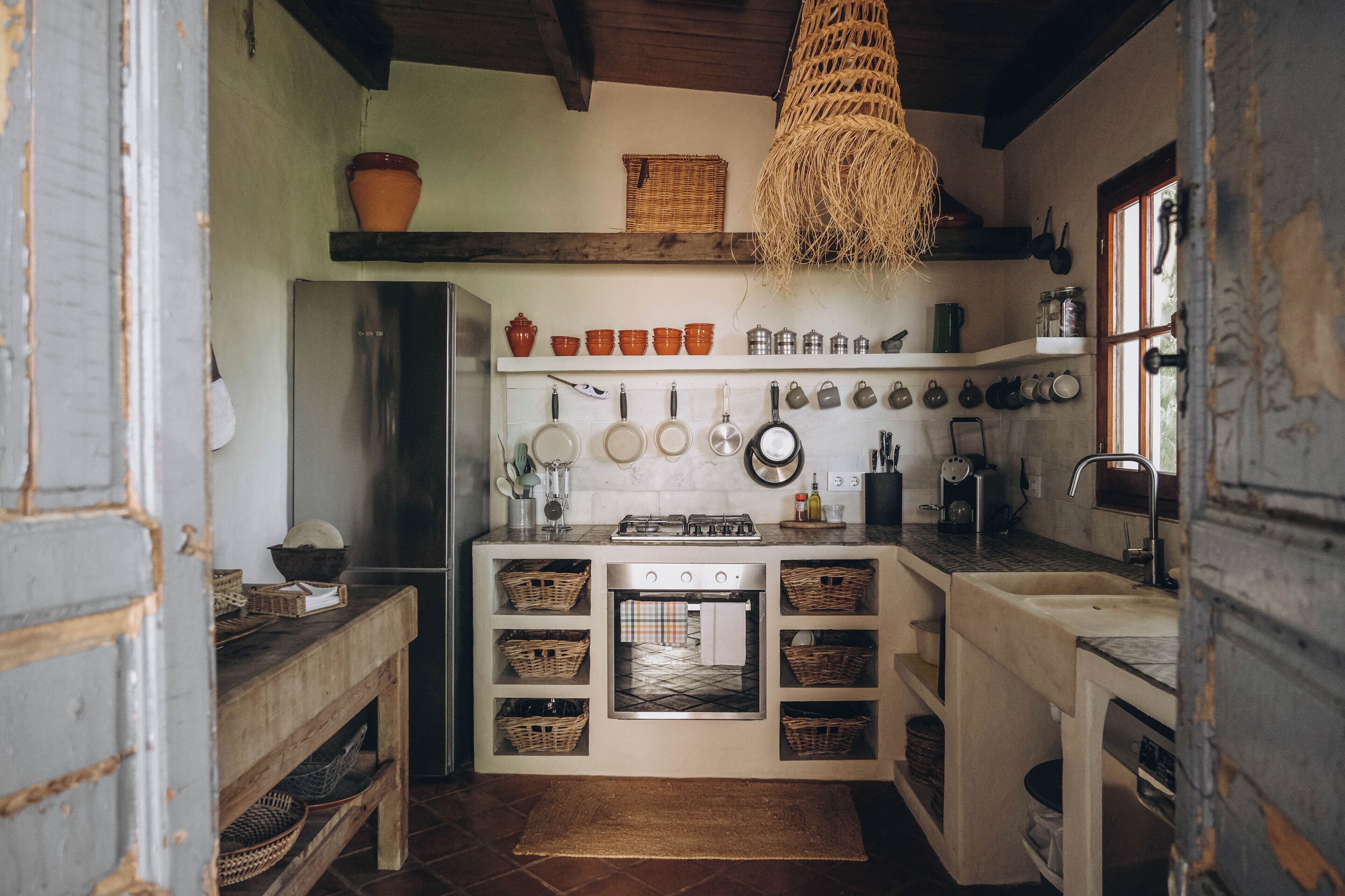 Une cuisine compacte dotée d’un four encastré, d’un porte-casseroles suspendu et d’un plafond en bois rustique.