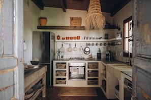 A compact kitchen with a built-in oven, a hanging pot rack, and a rustic wooden ceiling.