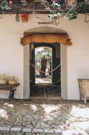 A doorway leading to a stone-paved area with a rustic wooden table and two ceramic pots.