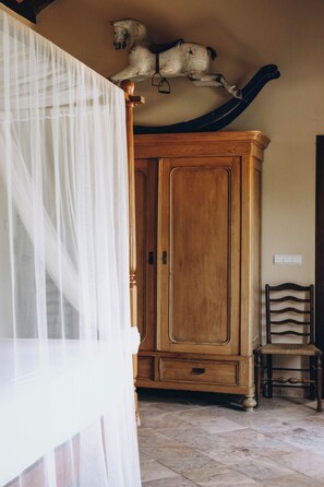 A room with a wooden wardrobe, a chair, and a bed with a sheer curtain.