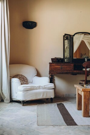 A room with a white armchair, a wooden dresser, a mirror, and a small wooden table.
