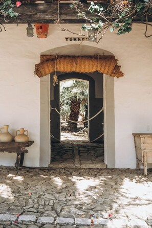 A doorway leading to a stone-paved area with a rustic wooden table and two ceramic pots.