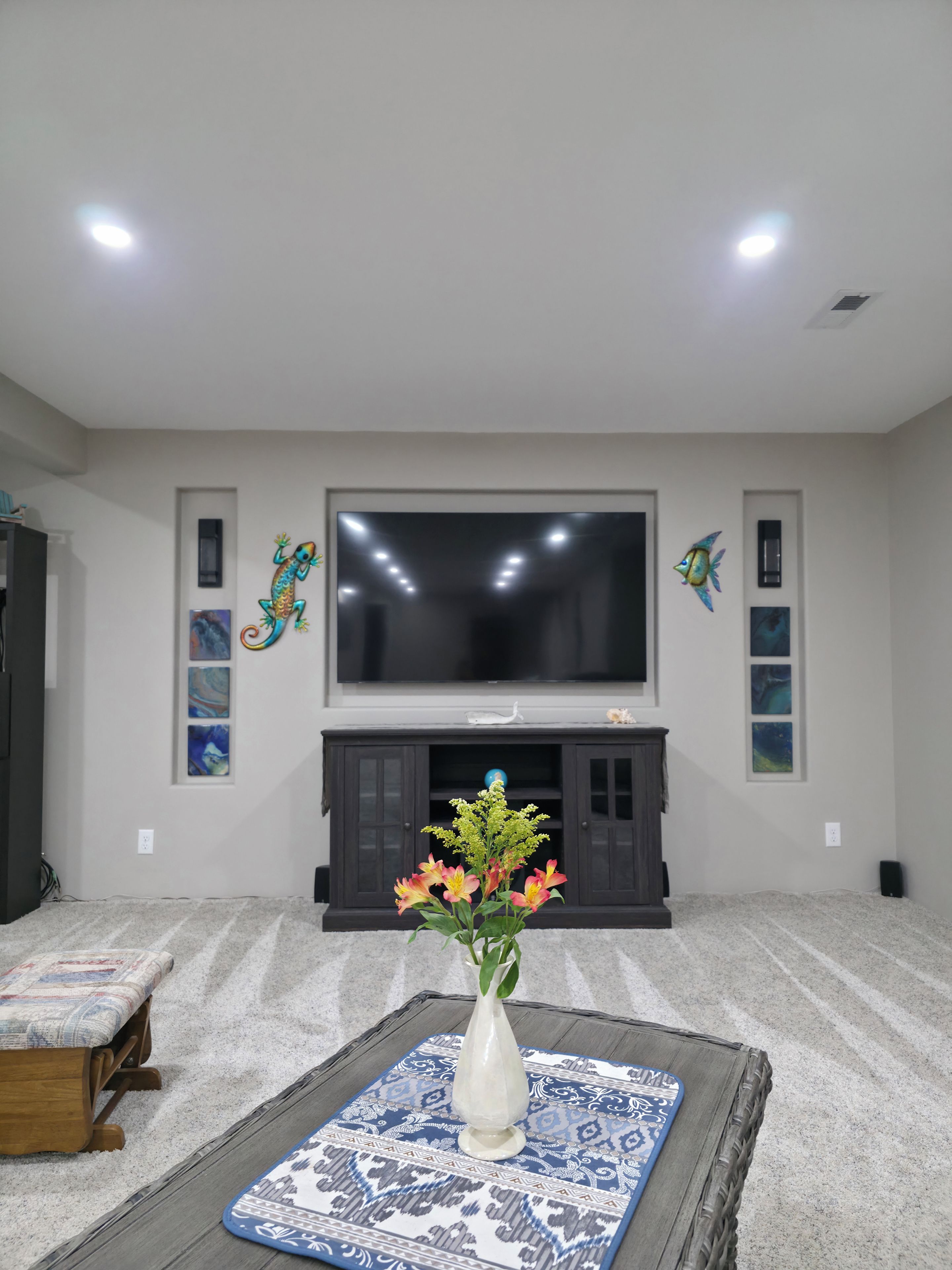 Una sala de estar con un televisor de pantalla plana, arte decorativo en la pared y un jarrón con flores sobre una mesa estampada.