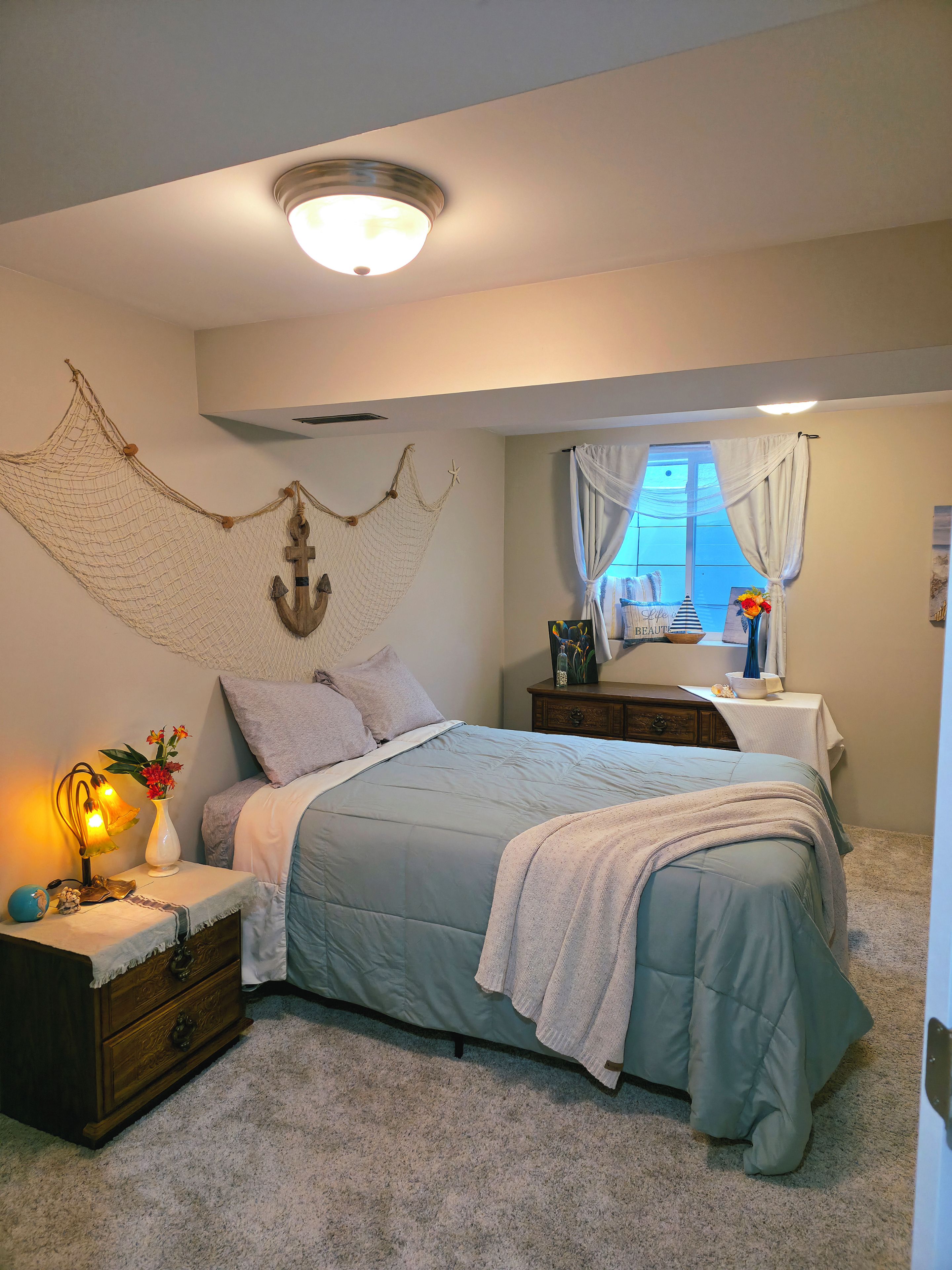 A bedroom with a bed, nightstand, dresser, and a window with curtains.