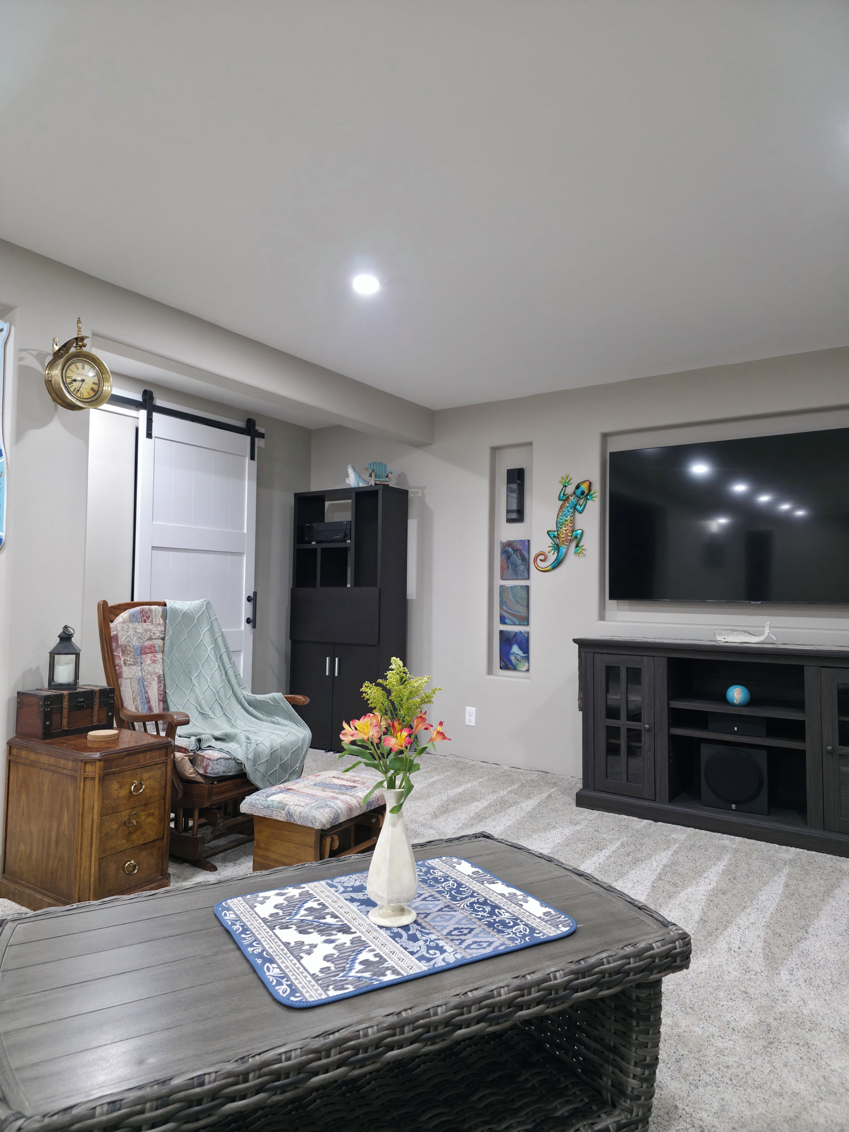 A living room with a television, a clock, a bookshelf, and a decorative wall piece.