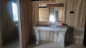 Een badkamer met een houten wand, een witte wastafel met spiegel, en een douchehoek.