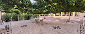 An outdoor seating area with a mosaic floor, a central table, and a pergola covered with grapevines.