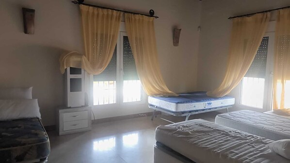 A bedroom with two beds, a bedside table, a wardrobe, and a window with curtains.