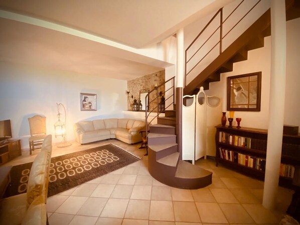 A living room with a curved staircase, a sofa, a coffee table, and a bookshelf.