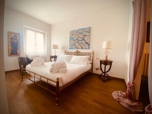 Une chambre d’hôtel comprenant un lit, deux tables de chevet, une chaise, une fenêtre et des œuvres d’art accrochées aux murs.