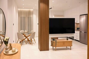 Ein modernes Wohnzimmer mit einem Glastisch, einem Holztisch und einem an der Wand befestigten Flachbildfernseher.