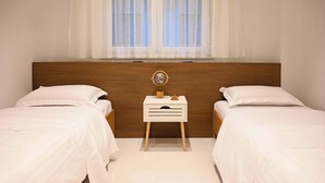 A bedroom with two single beds, a wooden headboard, a bedside table with a globe and a lamp, and a window with sheer curtains. - Light & Kozy Residence - Jacuzzi Lux Stay in Patra (Patra)