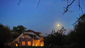 A house with a prominent moon in the sky, surrounded by trees.