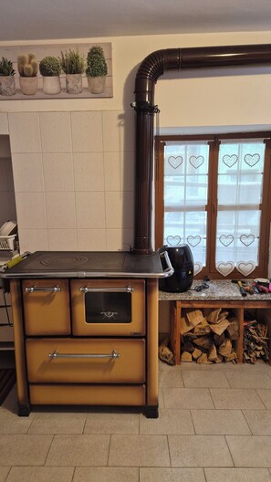 A kitchen with a stove, a wooden bench, and a window with heart-shaped decorations. - Graziosa casa di montagna (Noasca)