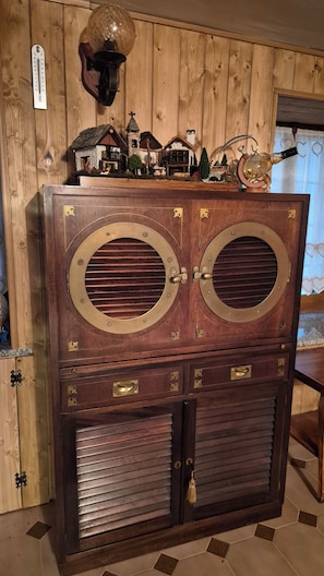 A wooden cabinet with two large circular doors, a small house model on top, and a thermometer on the wall. - Graziosa casa di montagna (Noasca)