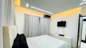 Quarto moderno com cama, cortinas, ar condicionado, televisão e mesa de cabeceira.