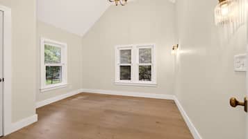 Une pièce dotée d’un plancher en bois, de deux fenêtres équipées de stores, d’un lustre et d’un luminaire fixé au mur.