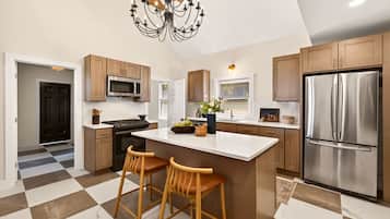 A modern kitchen with a central island, stainless steel appliances, wooden cabinets, and a chandelier.