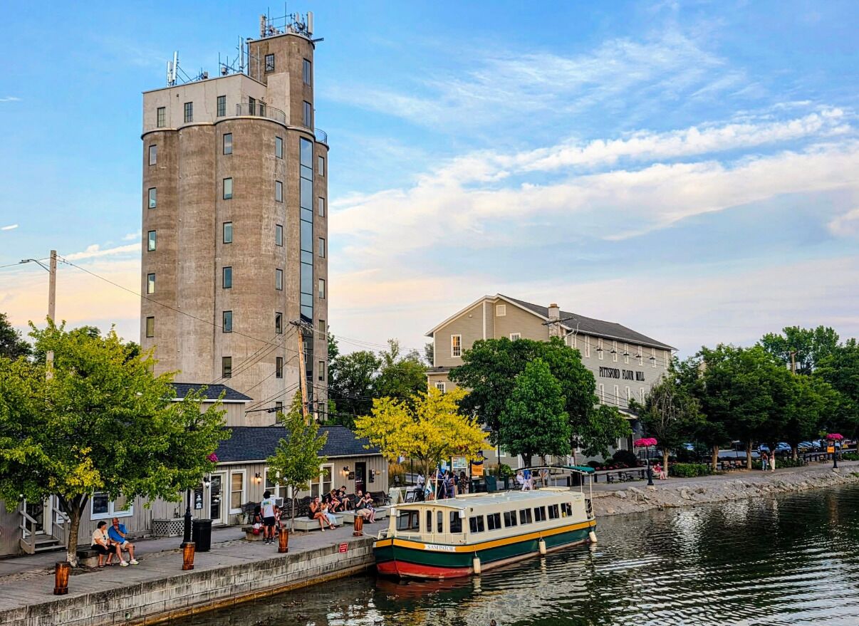 Une promenade au bord de la rivière, avec un grand immeuble, un bateau et des personnes sur le trottoir.