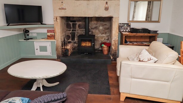 Ein gemütliches Wohnzimmer mit Kamin aus Stein, einem flachbildfernseher über einem Regal, einem bequemen Sofa und einem kleinen runden Tisch.