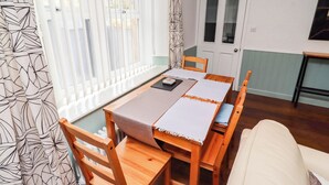 Ein Essbereich mit einem Holztisch und Stühlen, einer weißen Tischdecke und Blick durch ein Fenster mit Jalousien.