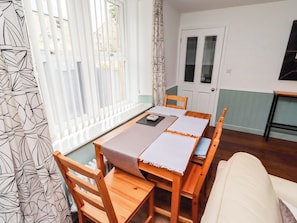 Ein Essbereich mit einem Holztisch und Stühlen, einer weißen Tischdecke und Blick durch ein Fenster mit Jalousien.