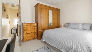 Ein Schlafzimmer mit einem Bett, einem Holzschrank, einer Kommode, einem Spiegel und einer Tür.
