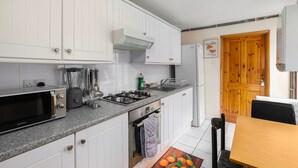 Eine kompakte Küche mit weißen Schränken, einem Gasherd, einem Backofen, einer Mikrowelle und einem Kühlschrank.
