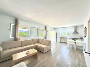 A modern living room with a sectional sofa, a dining table, and a kitchen area with a stove and refrigerator. - El Bancal Farm (AN)