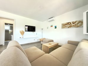 Uma sala de estar moderna com televisão de tela plana, sofá, mesa de centro e um quadro na parede.