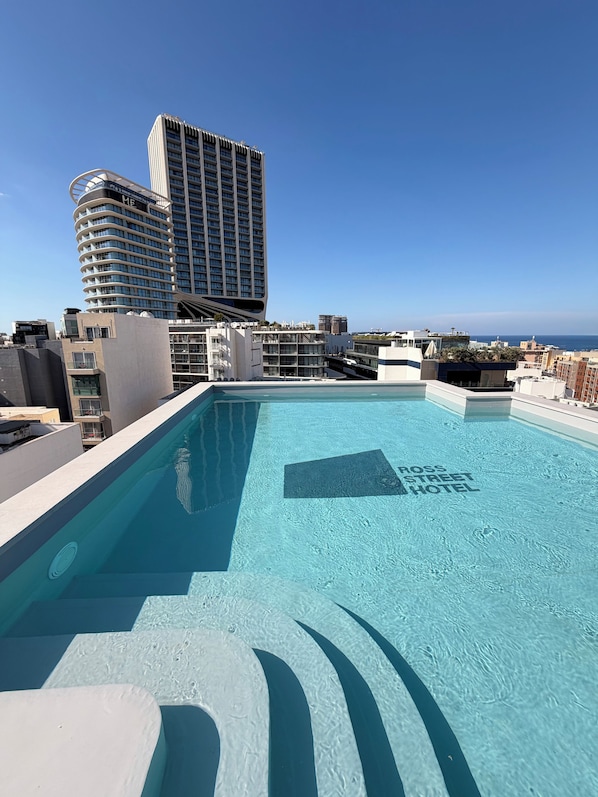 A rooftop pool with clear blue water, surrounded by modern buildings and a view of the ocean. - Ross Street Hotel (St. Julian's)