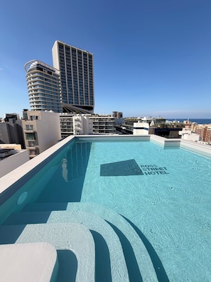 Una piscina en la azotea con agua azul cristalina, rodeada de edificios modernos y vistas al océano.
