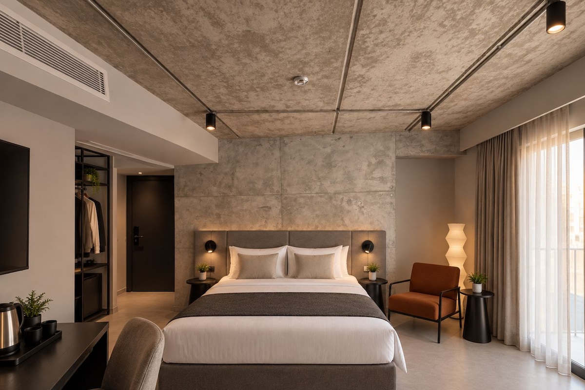 Una habitación de hotel moderna con una cama grande, un escritorio, una silla y vistas de la ciudad a través de la ventana.