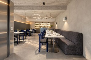 Un interior de restaurante moderno con una mesa larga, sillas azules y un banco acolchado gris.