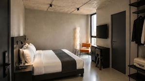 A modern bedroom with a large bed, a desk, a chair, a wardrobe, and a TV. - Ross Street Hotel (San Ġiljan)