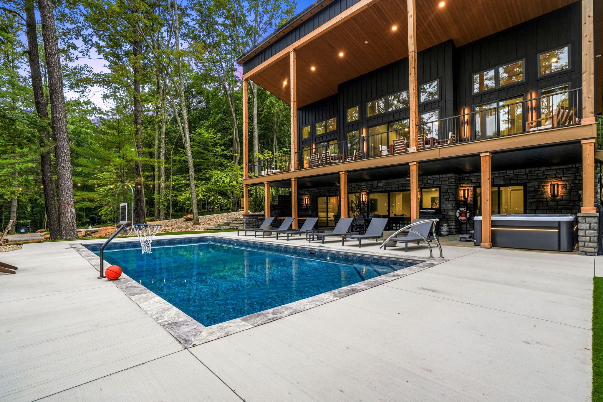 A modern outdoor pool area with a clear blue pool, lounge chairs, and a two-story building with large windows.