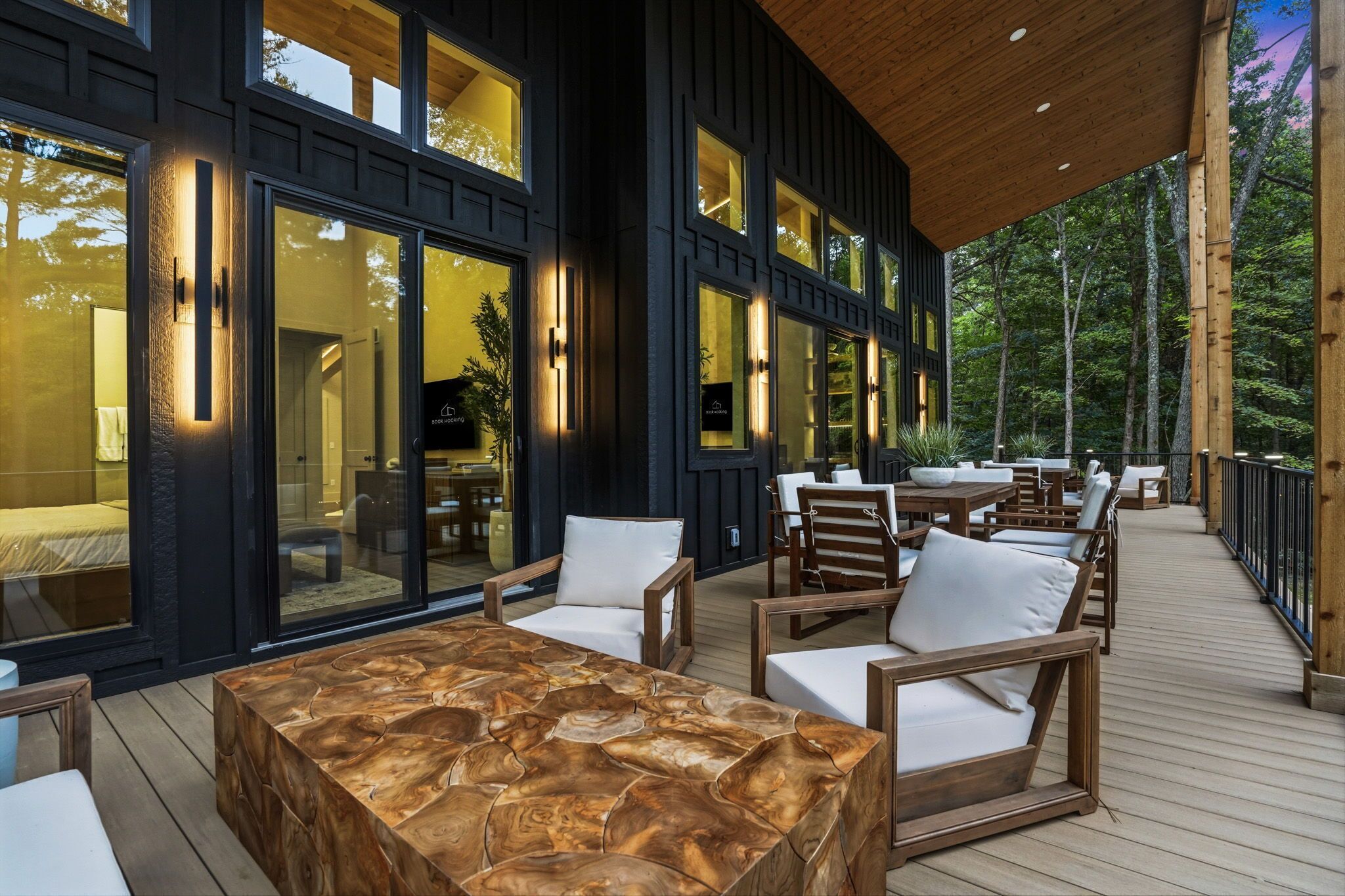 A modern outdoor deck with wooden furniture and glass doors leading to a room.