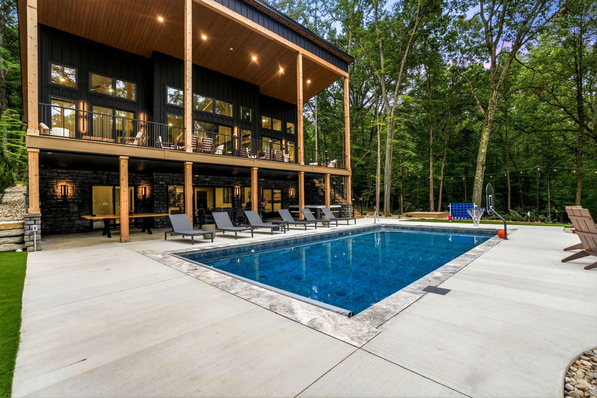 Ein modernes, zweistöckiges Gebäude mit Swimmingpool, Sitzgelegenheiten im Freien und bewaldeter Umgebung.