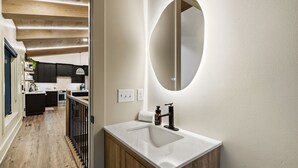 Una cocina moderna con armarios oscuros, una encimera blanca y un espejo redondo sobre el lavabo.