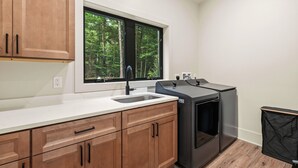 Una cocina con armarios de madera, horno negro, encimera blanca y ventana con vistas a árboles.